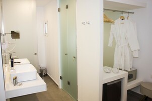 Casa de banho moderna com lavatório branco, espelho e cabine de duche em vidro. Dois roués brancos pendurados numa estante.