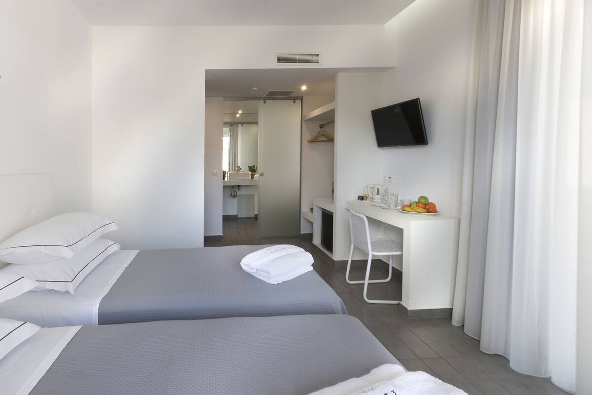 A hotel room with two beds, a desk, a TV, and a bathroom visible through an open door.
