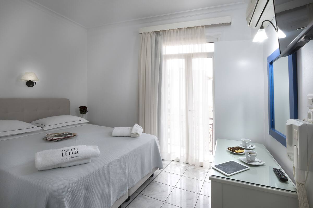 A hotel room with a bed, a bedside table with a remote control, a tablet, and a cup of coffee.