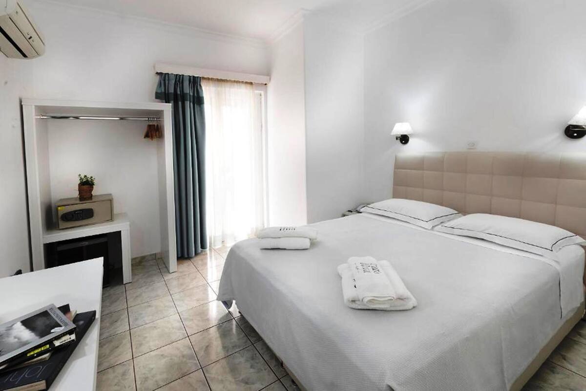 A hotel room with a bed, a bedside table, a wardrobe, and a window with curtains.