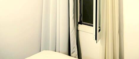 Una habitación con ventana, cortinas blancas y aire acondicionado de pared.