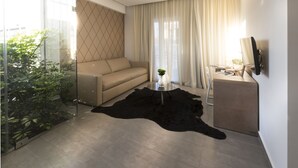 Un soggiorno moderno con un divano beige, una parete divisoria in vetro, un tappeto nero, un tavolino rotondo con un vaso e un televisore su un mobile.