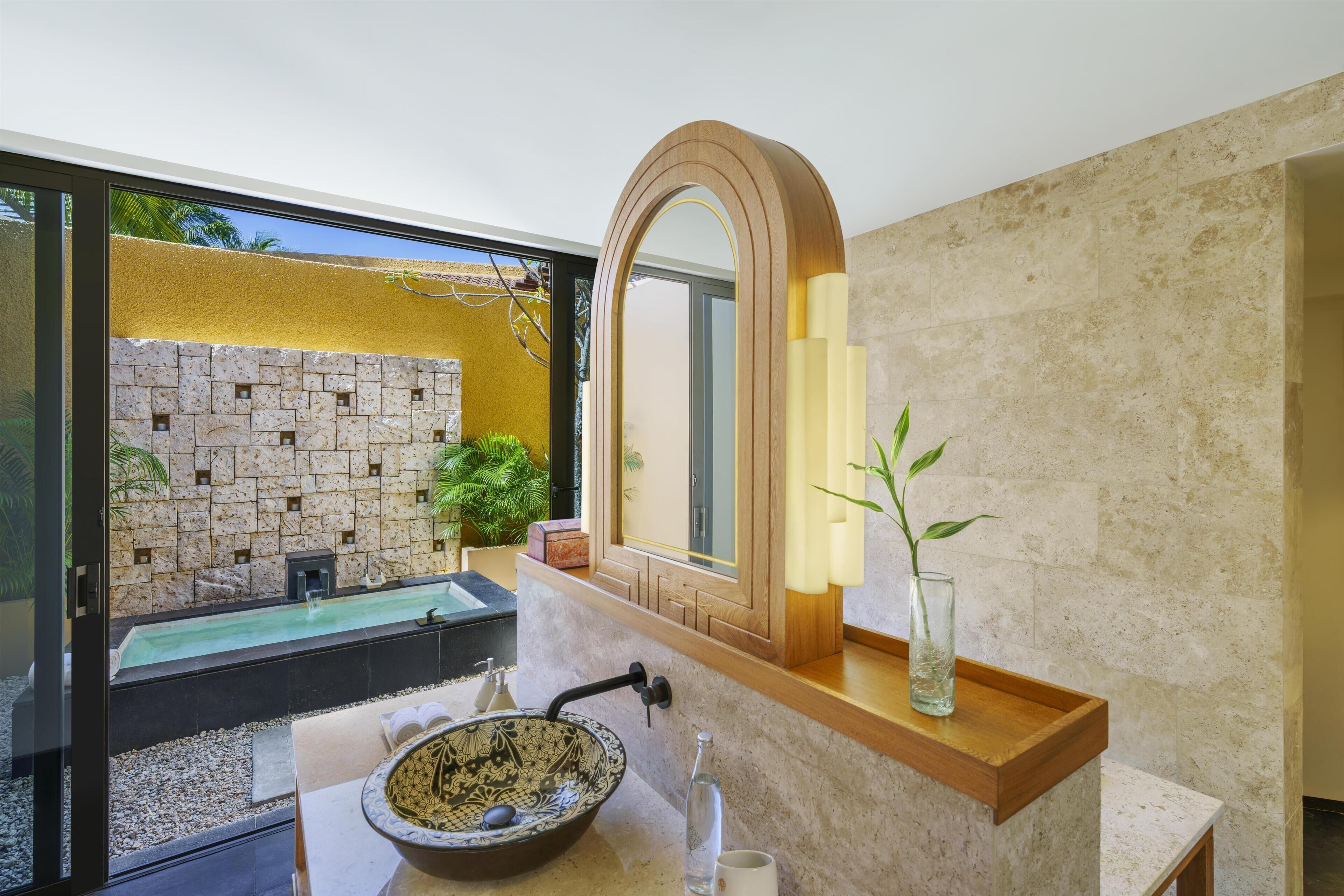 Un baño con pared de piedra, un lavamanos, un espejo y una planta pequeña.