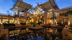 A hotel with a traditional architectural style, featuring a central courtyard with a reflective pool, surrounded by lush greenery and illuminated by hanging lights.