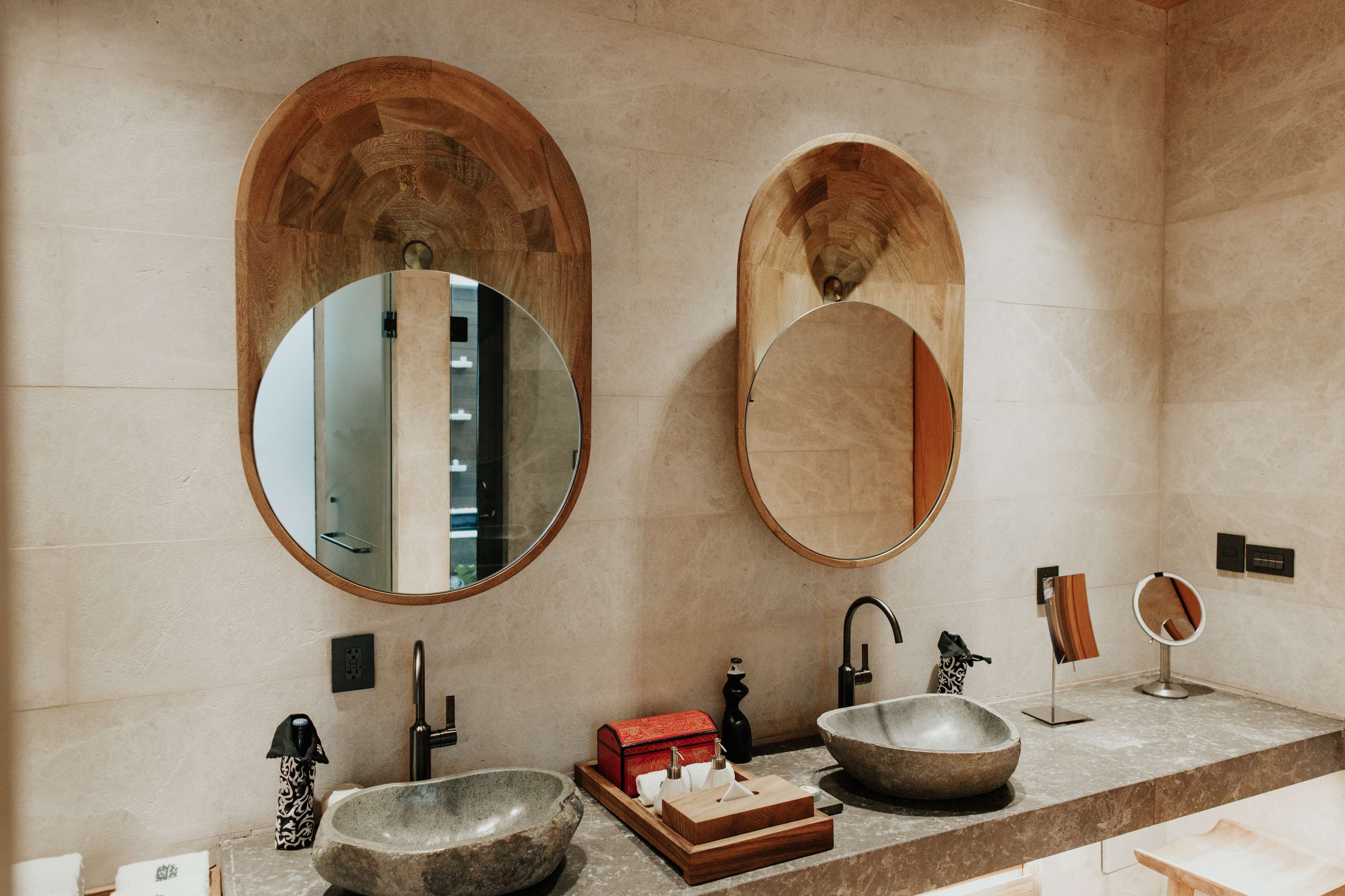 Un baño con dos espejos ovalados grandes, un lavabo de piedra y un tocador de madera.