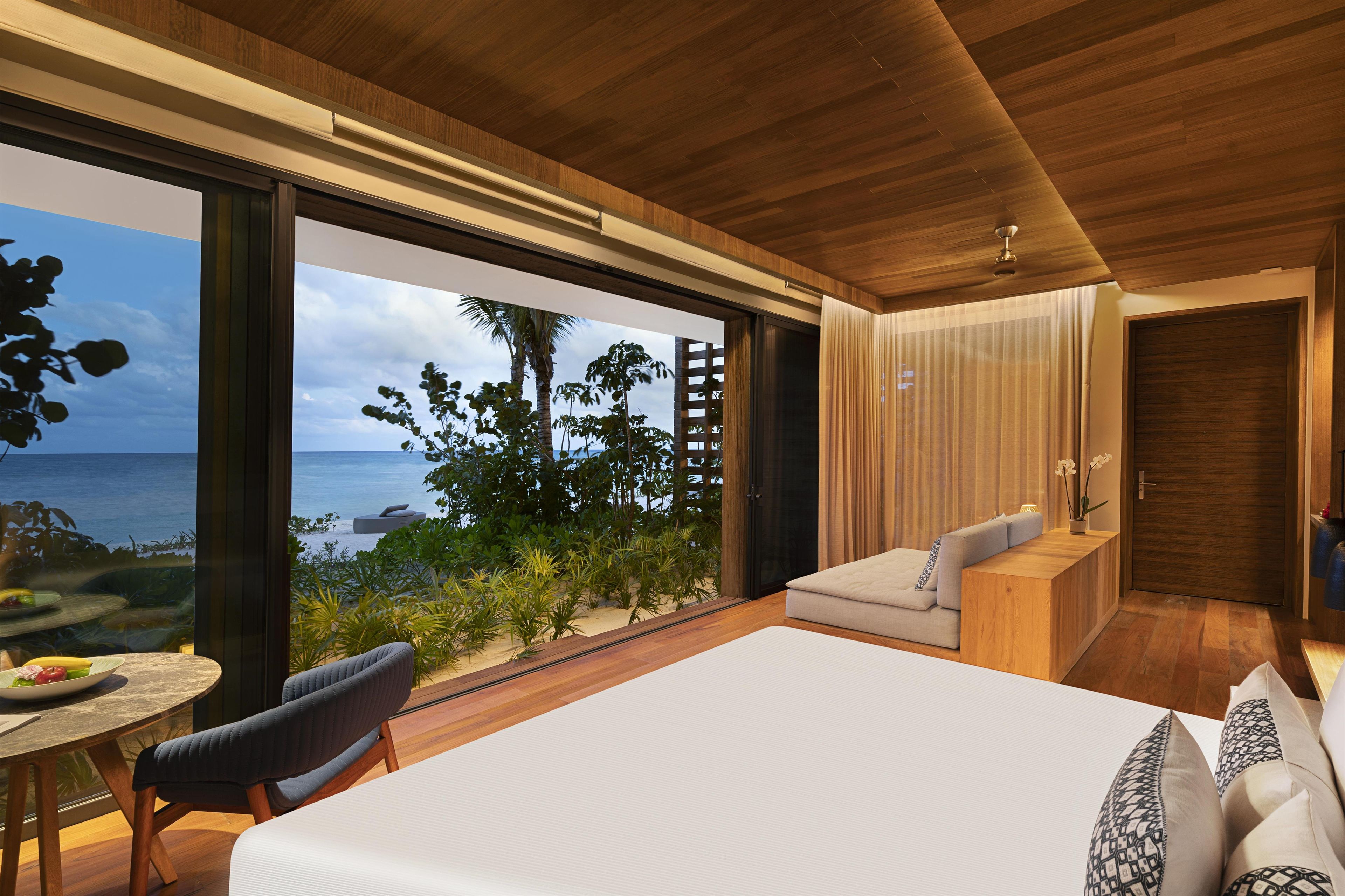 A modern bedroom with a large bed, a seating area, and a view of the sea.