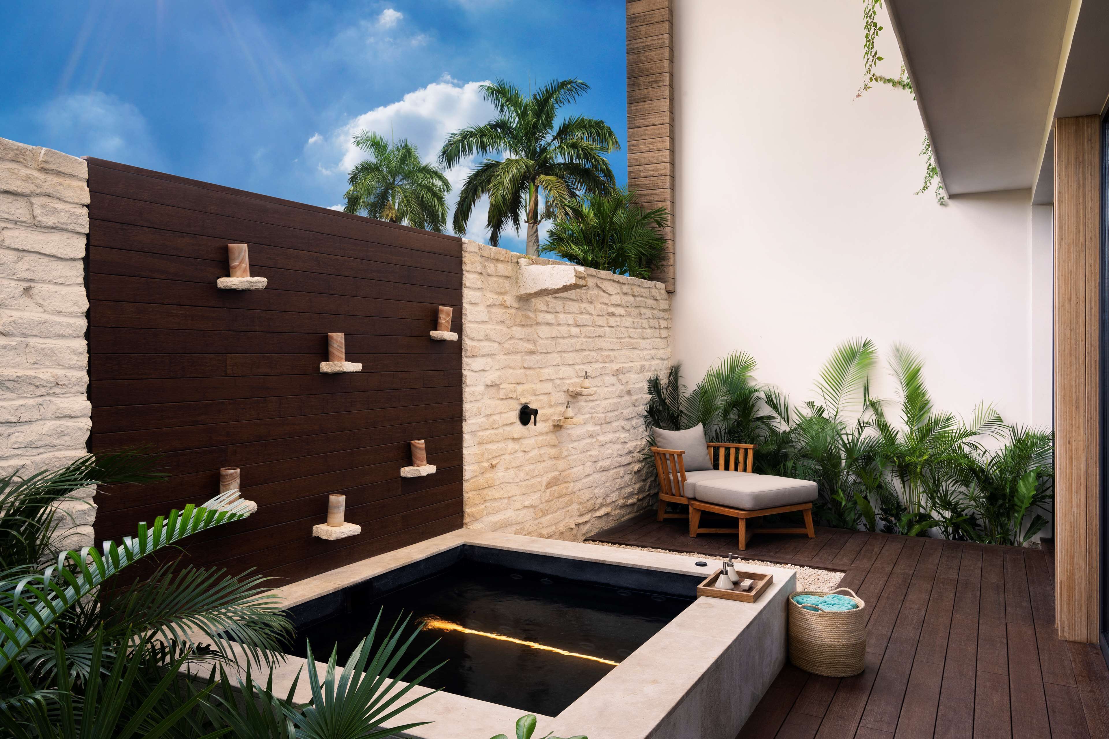 A spa area with a hot tub, wooden and stone walls, a wooden deck, and a chair.