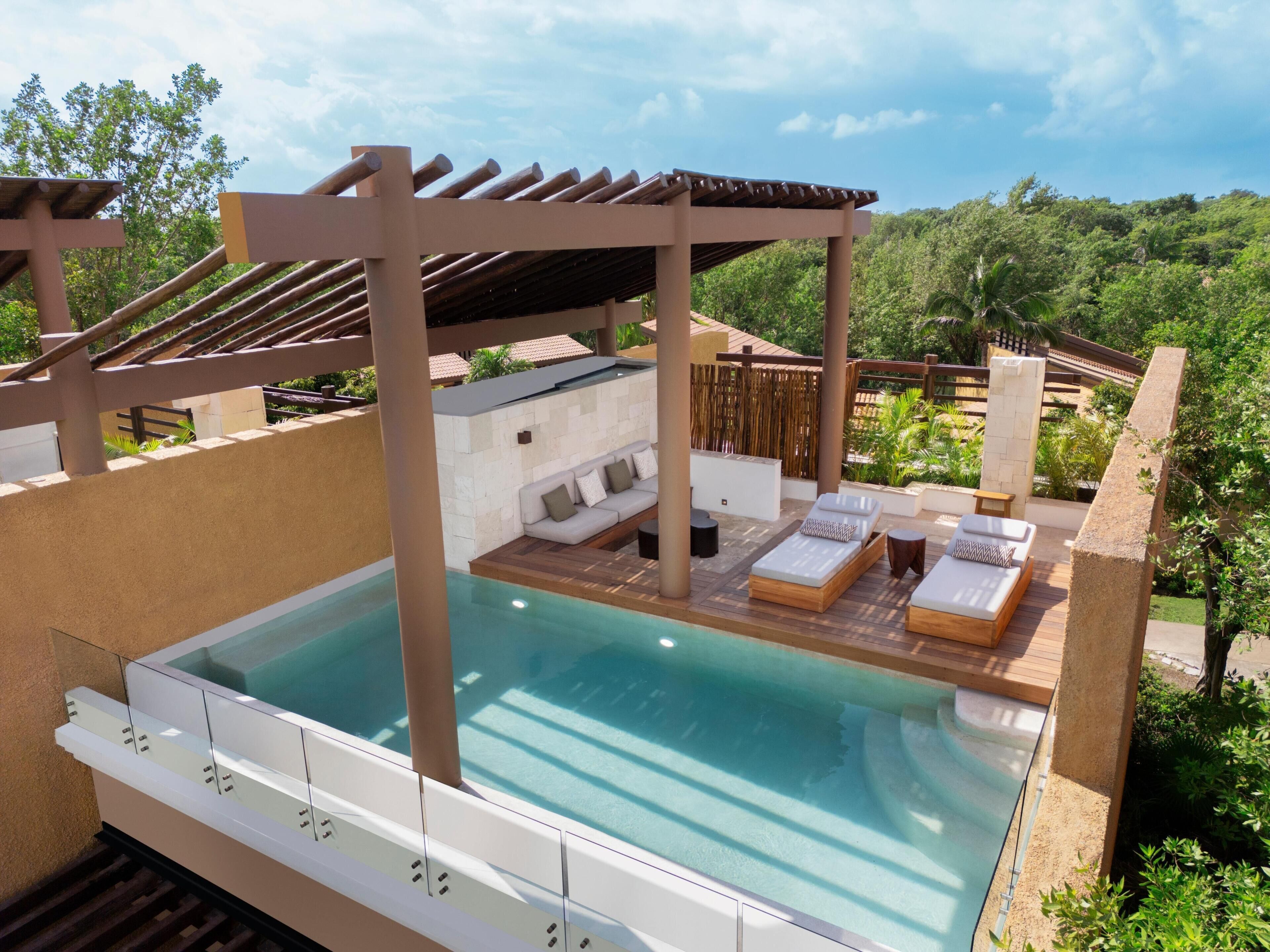 Een zwembad op het dak met een pergola, ligbedden en uitzicht op de groene omgeving.