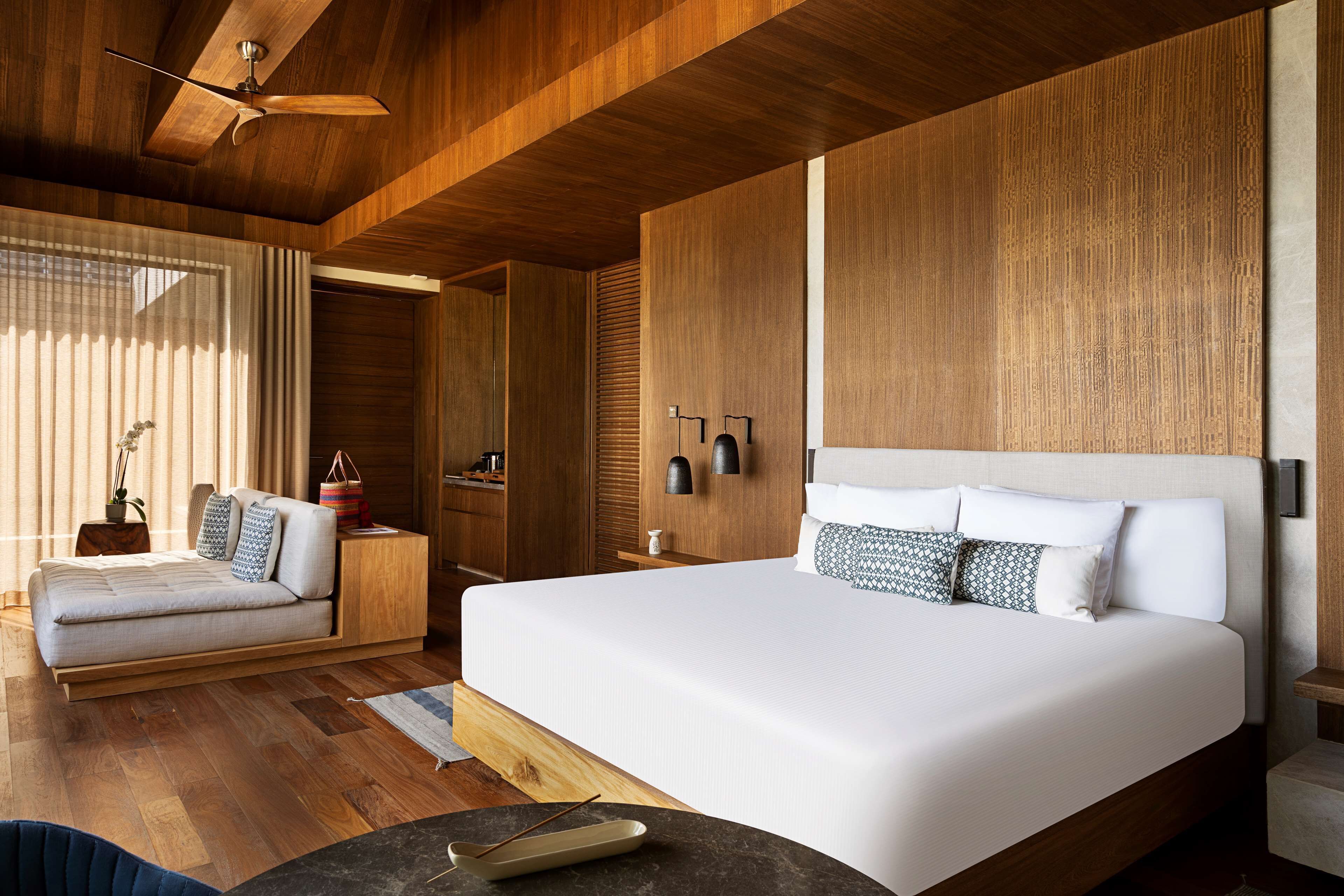 Un dormitorio moderno con una cama grande, techo de madera y un rincón de descanso con sofá.