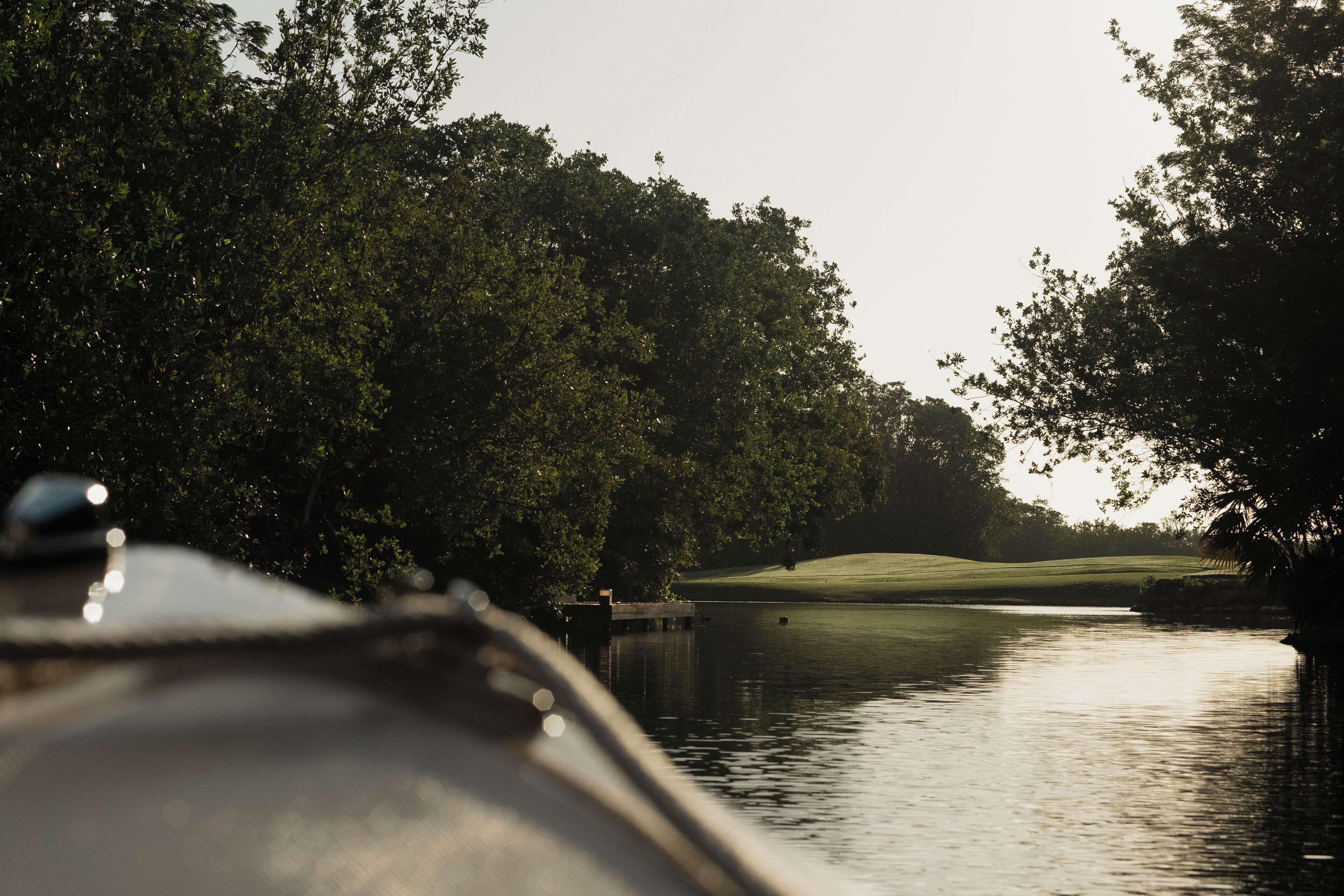 A body of water with a dock, surrounded by dense trees and a golf course in the background.
