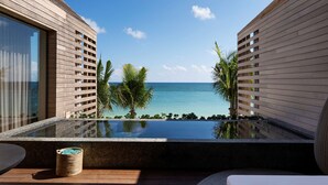 A modern infinity pool with a clear view of the ocean, wooden deck, and a wicker basket.