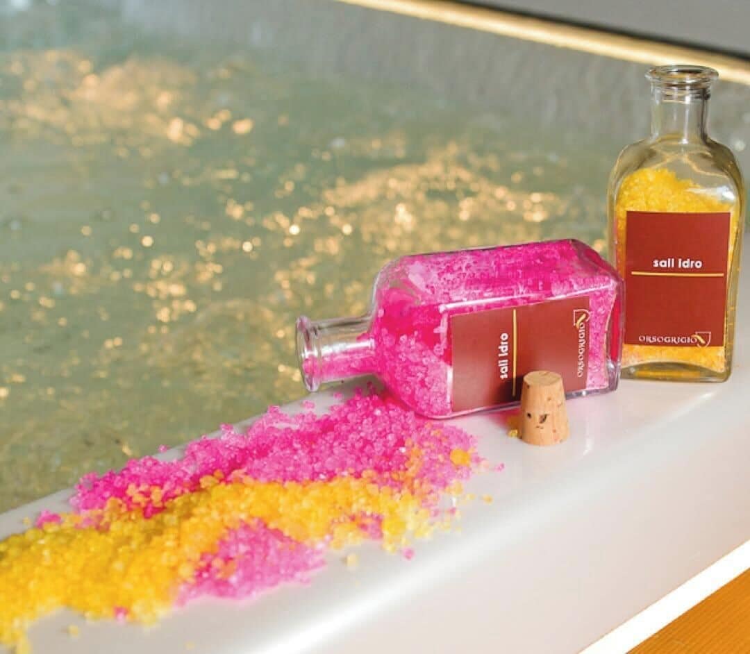 Une bouteille contenant une substance granulaire rose et jaune s’est renversée sur une surface blanche, à côté d’un bouchon et d’une bouteille étiquetée « sall idro ».