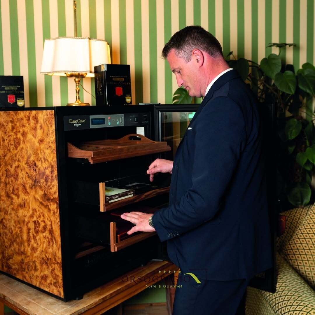 A man in a dark suit interacting with a wooden-built oven in a room with green-striped wallpaper.
