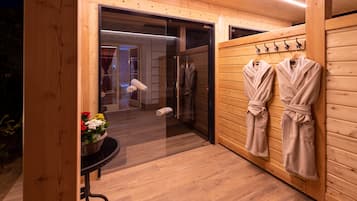 L’intérieur est en bois et une porte en verre donne accès à une salle de bain. Des serviettes et des peignoirs sont suspendus à des crochets.