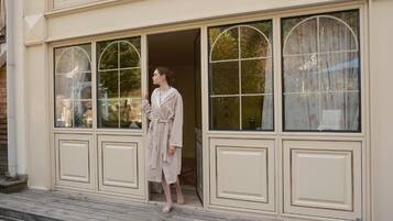 A person in a robe standing at a building entrance with large arched windows and a wooden deck.