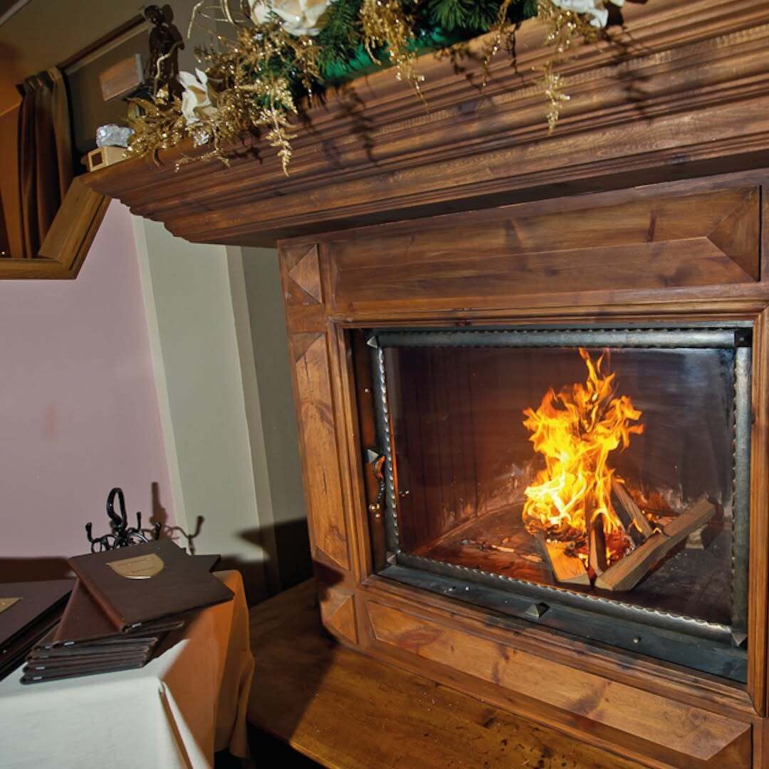A wooden fireplace with a glass door, a mantel with decorative items, and a table with books and a candle holder nearby.