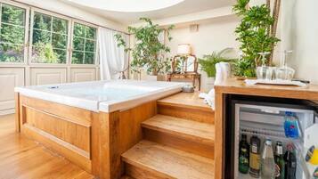 Habitación con una bañera de madera, un refrigerador lleno de bebidas y vistas a zonas verdes a través de amplios ventanales.