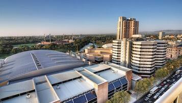 A modern building with a curved roof and multiple floors, surrounded by other buildings and a road with vehicles.