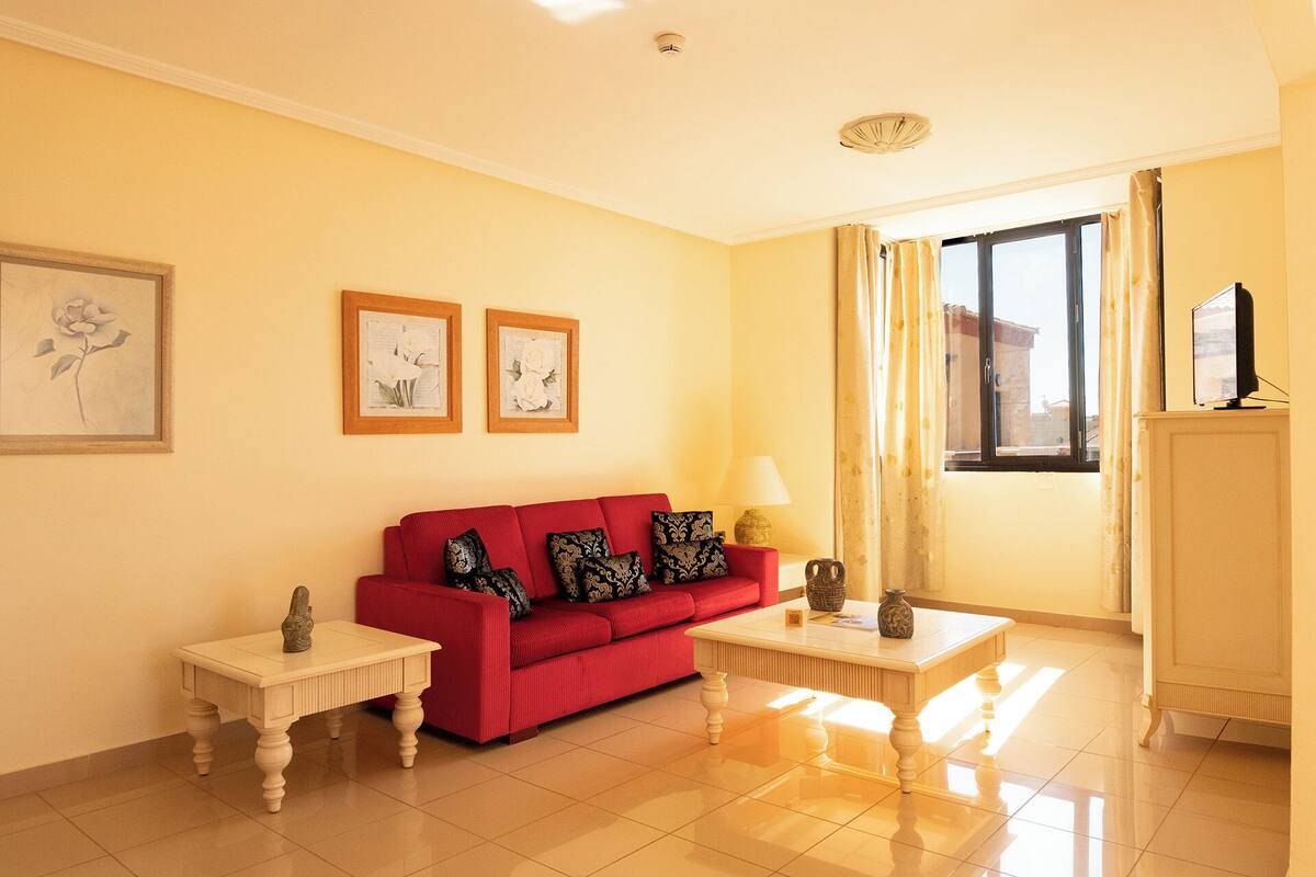A living room with a red sofa, two side tables, a lamp, and framed artwork on the wall.