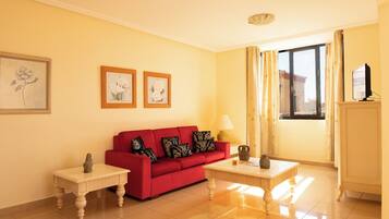 A living room with a red sofa, two side tables, a lamp, and framed artwork on the wall.