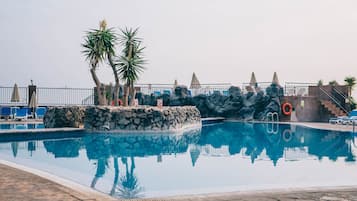 Una piscina al aire libre, sombrillas, sillones reclinables de piscina