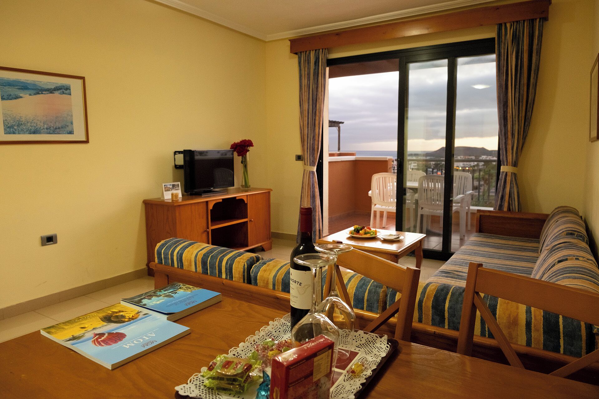 A living room with a sofa, a dining table with books, a TV, and a bottle of wine.