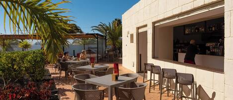An outdoor patio with tables and chairs, a bar area, and a view of the sea.