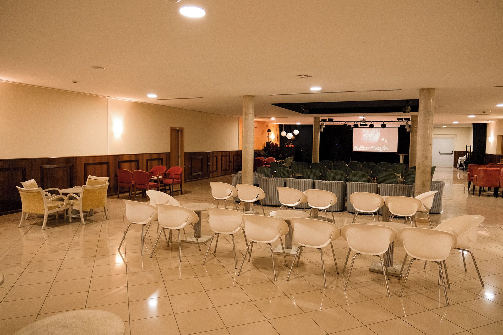 A conference room with rows of chairs, a stage with a screen, and a seating area with tables and chairs.
