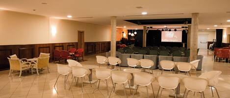 A conference room with rows of chairs, a stage with a screen, and a seating area with tables and chairs.