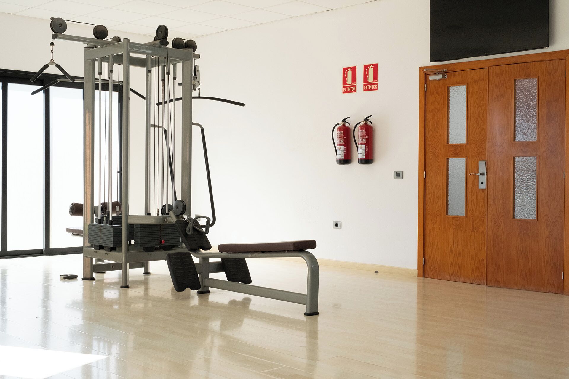Un gimnasio con una barra de dominadas, un banco y dos extintores en la pared.