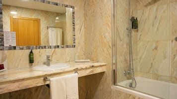 Un baño con tocador de mármol, lavamanos, espejo, ducha y toallero.