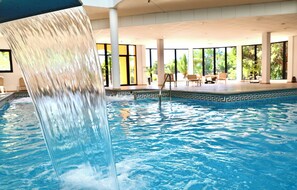 A swimming pool with a waterfall feature, indoor seating area, and large windows. - Grand Muthu Golf Plaza Hotel (San Miguel de Abona)