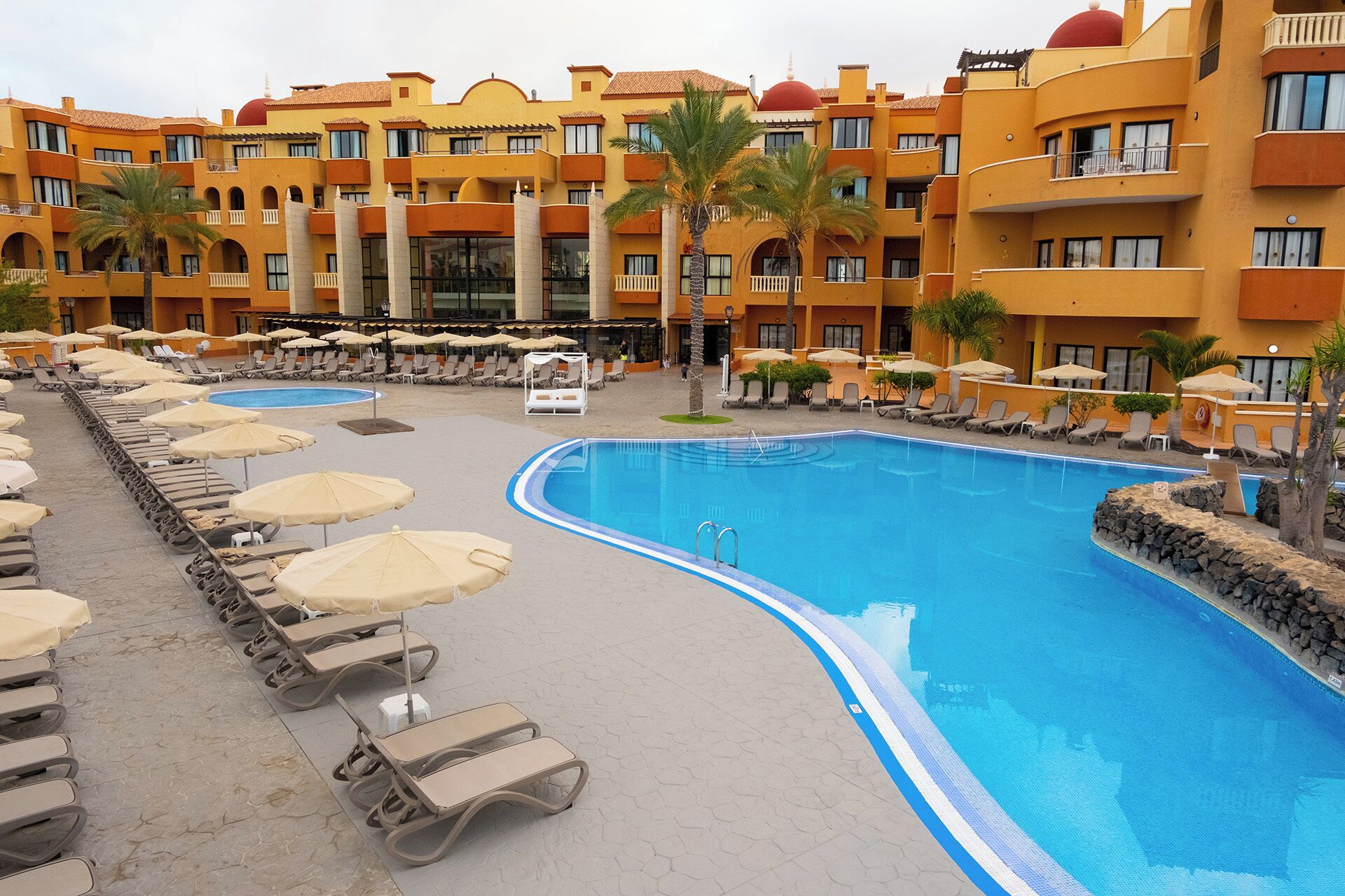 Un hotel con una piscina grande, sillas de descanso y sombrillas.