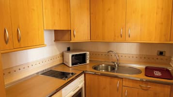Une cuisine compacte avec des meubles en bois, un four à micro-ondes encastré, un évier en acier inoxydable et un plateau rouge.