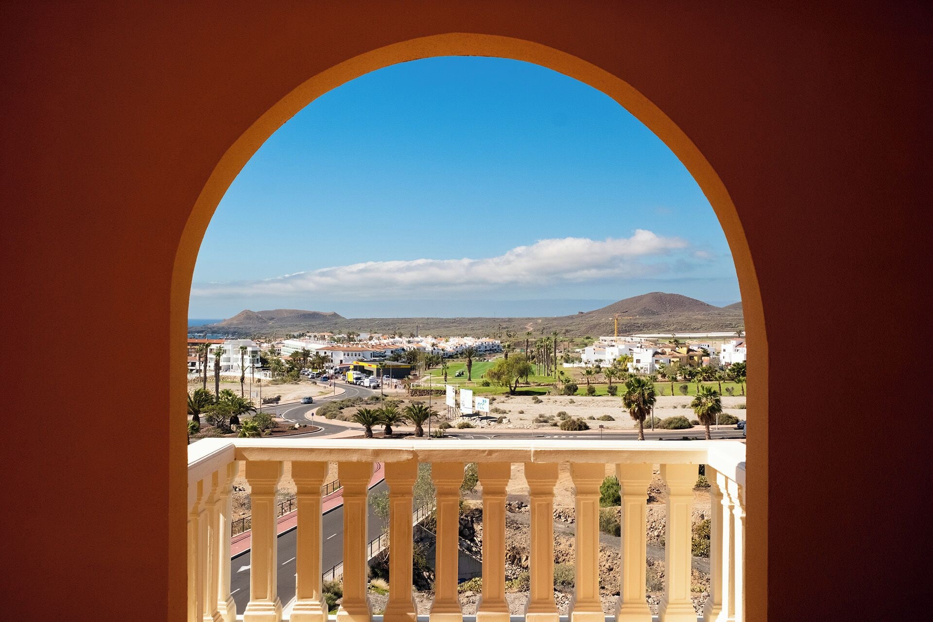 A view through an archway of a coastal town with buildings, roads, and mountains.