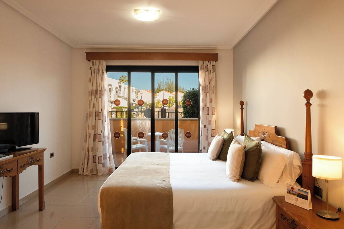 A hotel room with a bed, a TV, a desk, and a lamp.