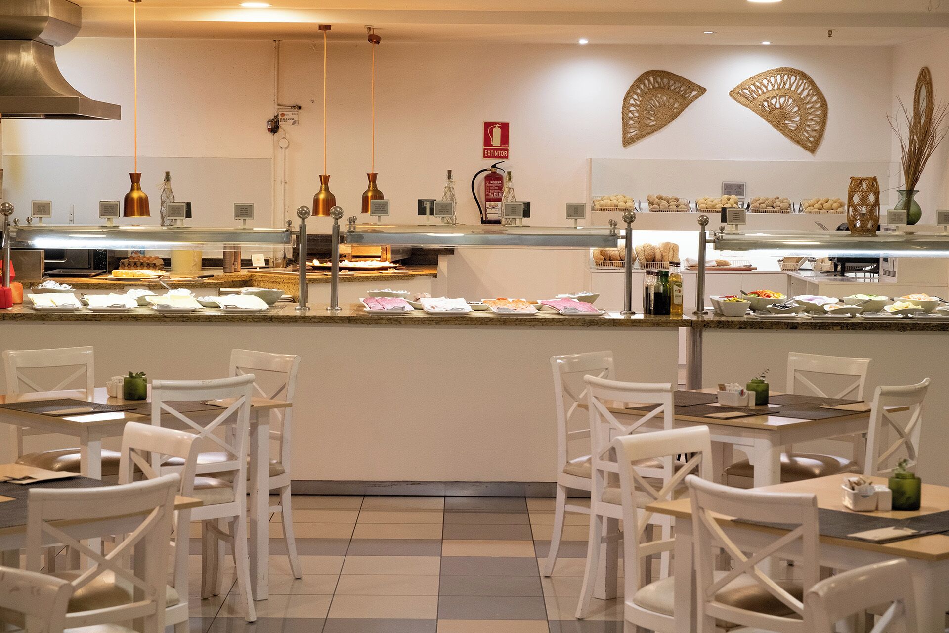 A restaurant with a buffet counter, white chairs, and a tiled floor.