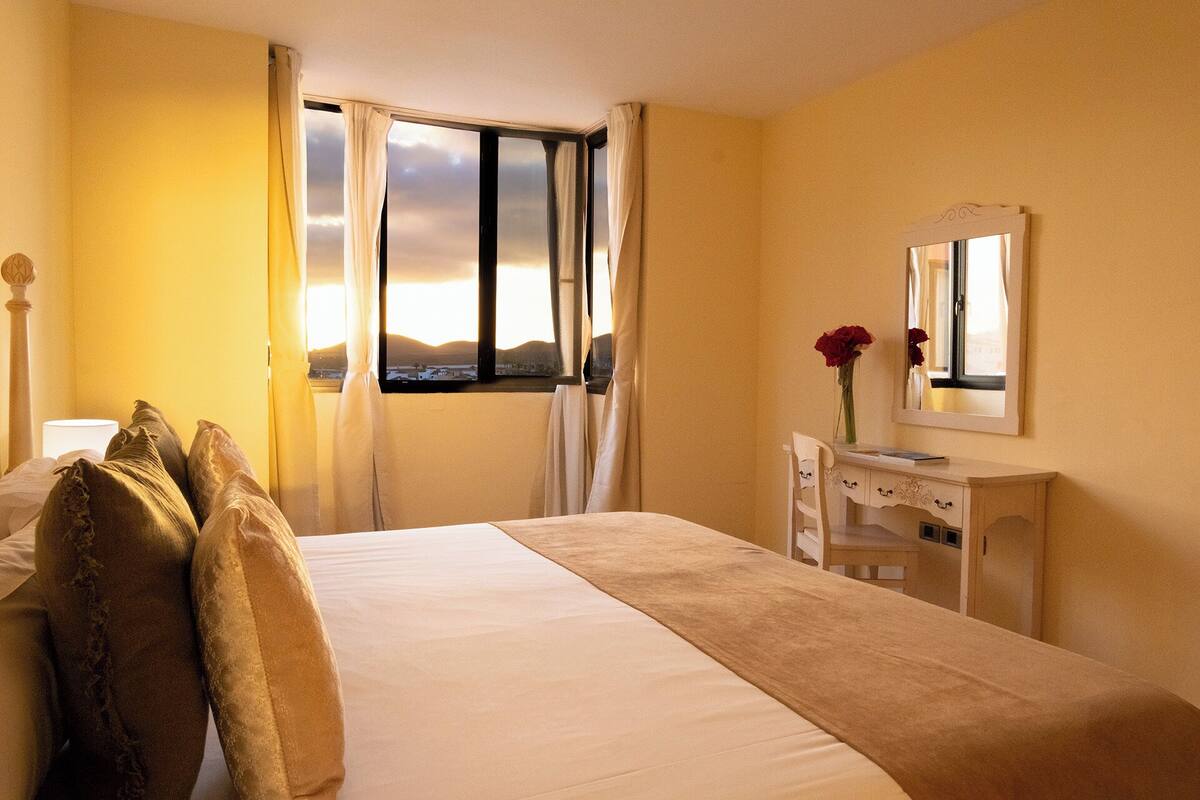 A hotel room with a bed, a desk, a mirror, and a window with curtains.