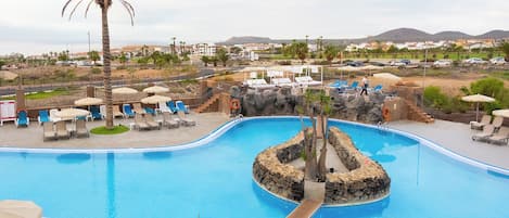 Una piscina con sillas de descanso y sombrillas, rodeada de un paisaje rocoso y palmeras.