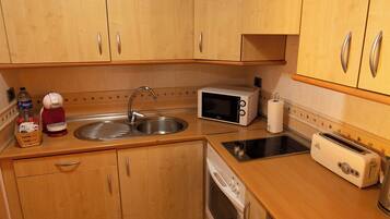 A compact kitchen with wooden cabinets, a stainless steel sink, a microwave, a toaster, and a dish drying rack.