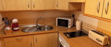 A compact kitchen with wooden cabinets, a stainless steel sink, a microwave, a toaster, and a dish drying rack.