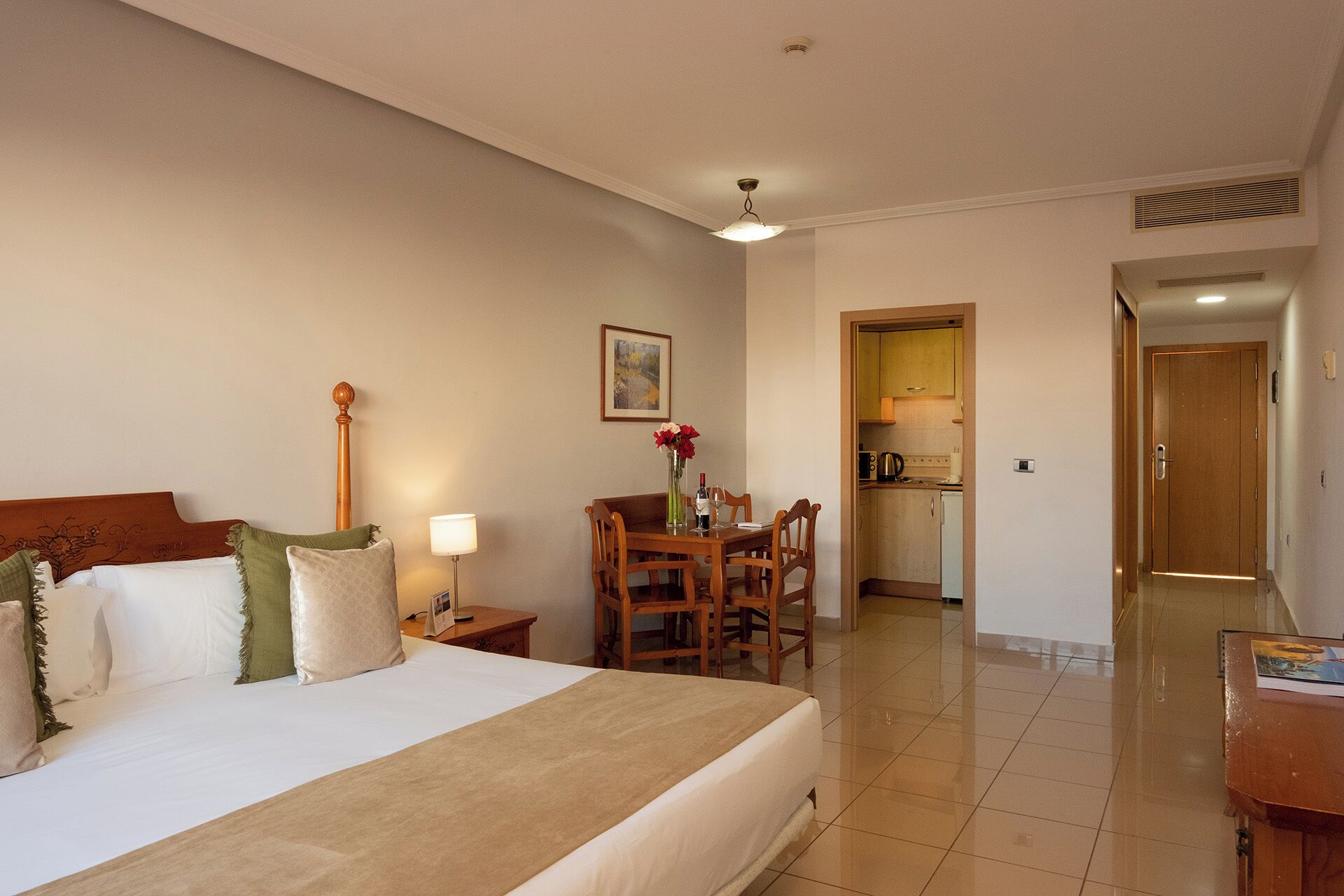 A hotel room with a bed, bedside table, lamp, and a dining area with chairs and a table.