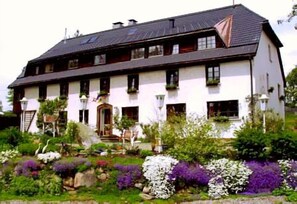 A large, two-story building with a sloped roof, multiple windows, and a well-maintained garden with various plants and flowers. - Hotel Das Landhaus (Hoechenschwand)