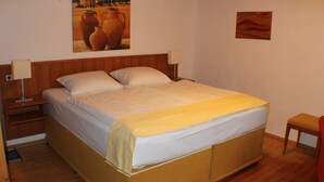 A single-bed room with a wooden headboard, two bedside lamps, a nightstand, and a small wooden chair. - Hotel Das Landhaus (Hoechenschwand)