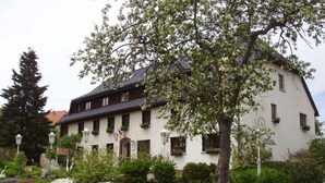 A white building with a sloped roof, multiple windows, and a garden with various plants and flowers. - Hotel Das Landhaus (Hoechenschwand)