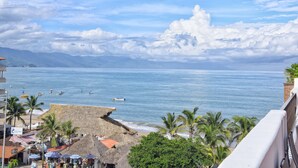 Vista costera con playa, cabañas de techo de paja, palmeras y cielo despejado.