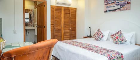 Un dormitorio con cama, un armario de madera, un baño con espejo y un cuadro en la pared.