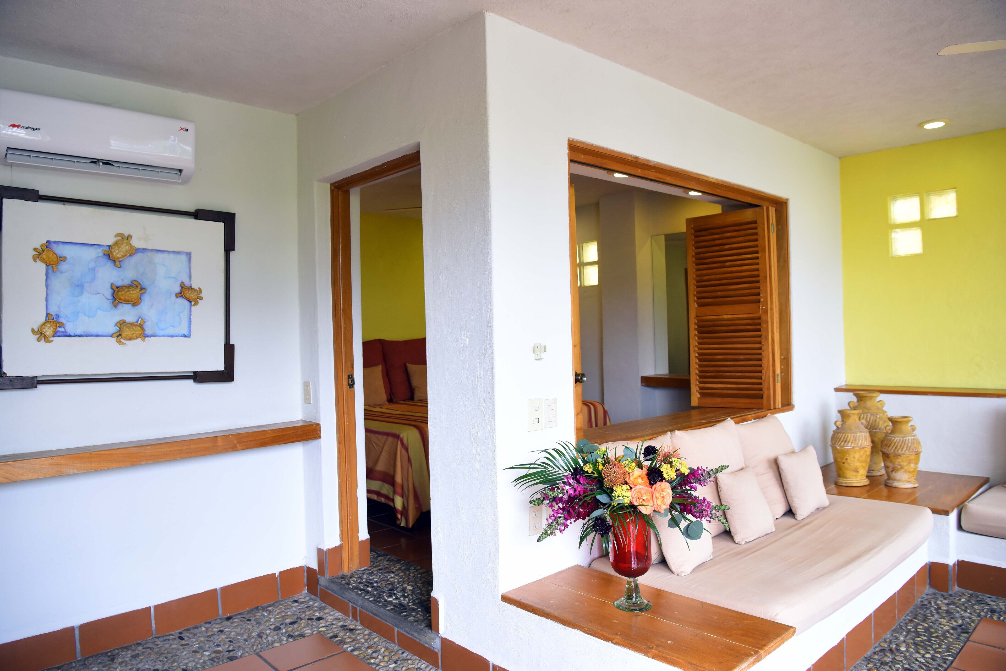 A room with a wooden bench, a vase with flowers, and a framed artwork on the wall.