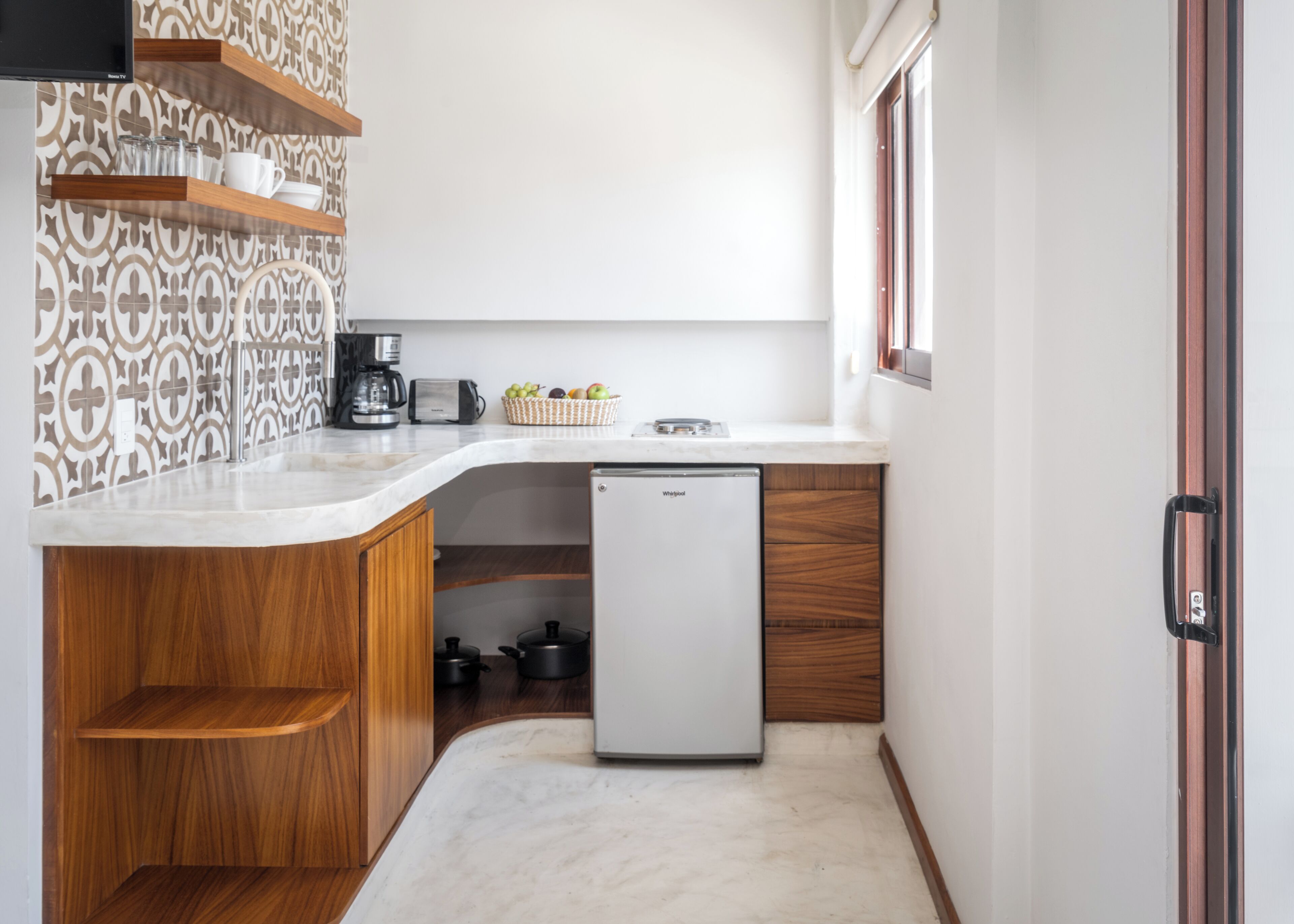 A compact kitchen with a built-in refrigerator, wooden cabinets, a marble countertop, and a patterned backsplash.