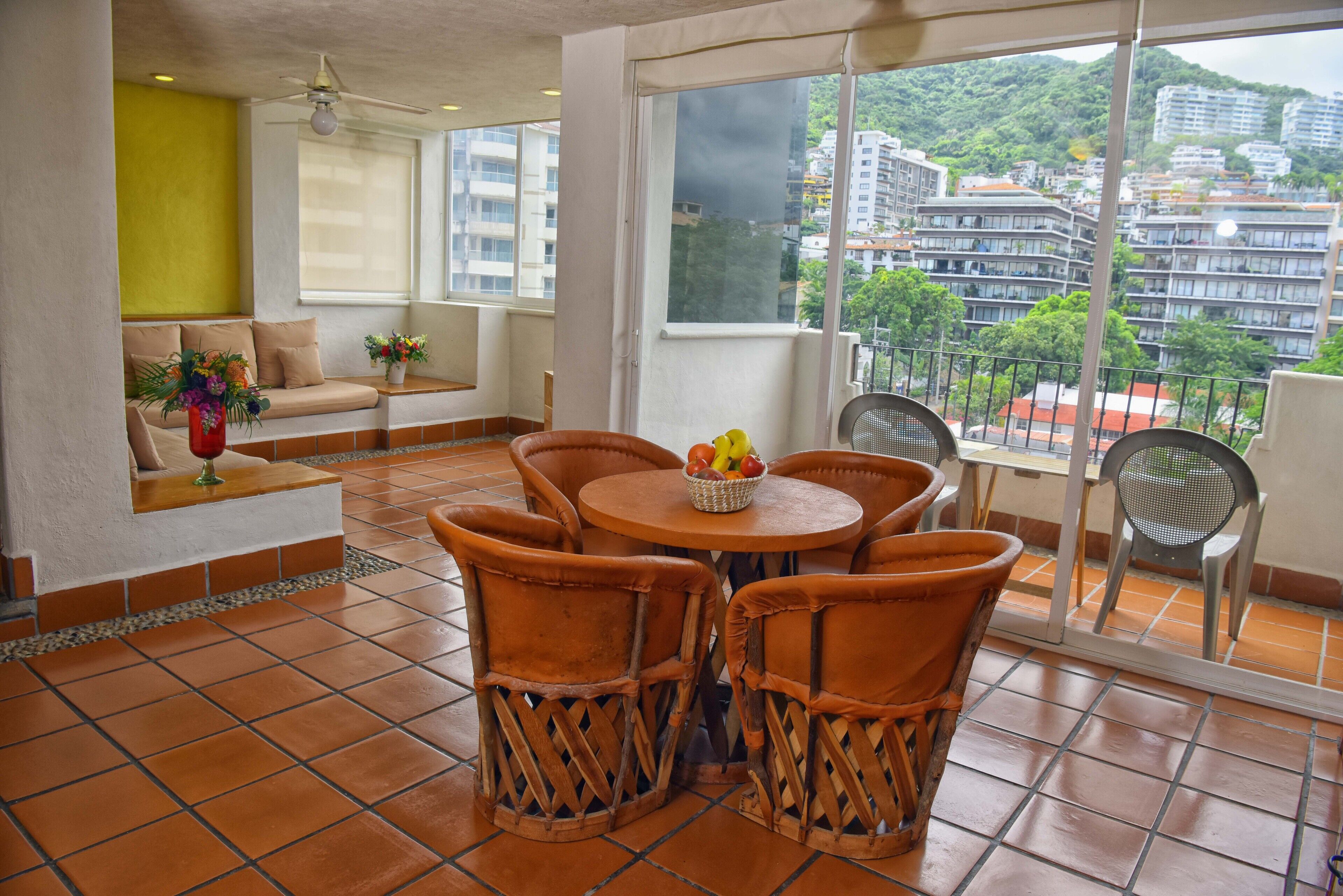 A balcony with a round table and wicker chairs, a sofa, and a potted plant.